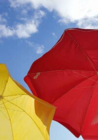 a red and yellow umbrella in the hot sun with a blue sky and white clouds