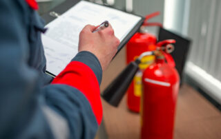An inspector filling out a fire safety compliance checklist next to fire extinguishers.