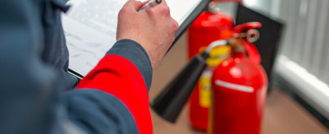 An inspector filling out a fire safety compliance checklist next to fire extinguishers.